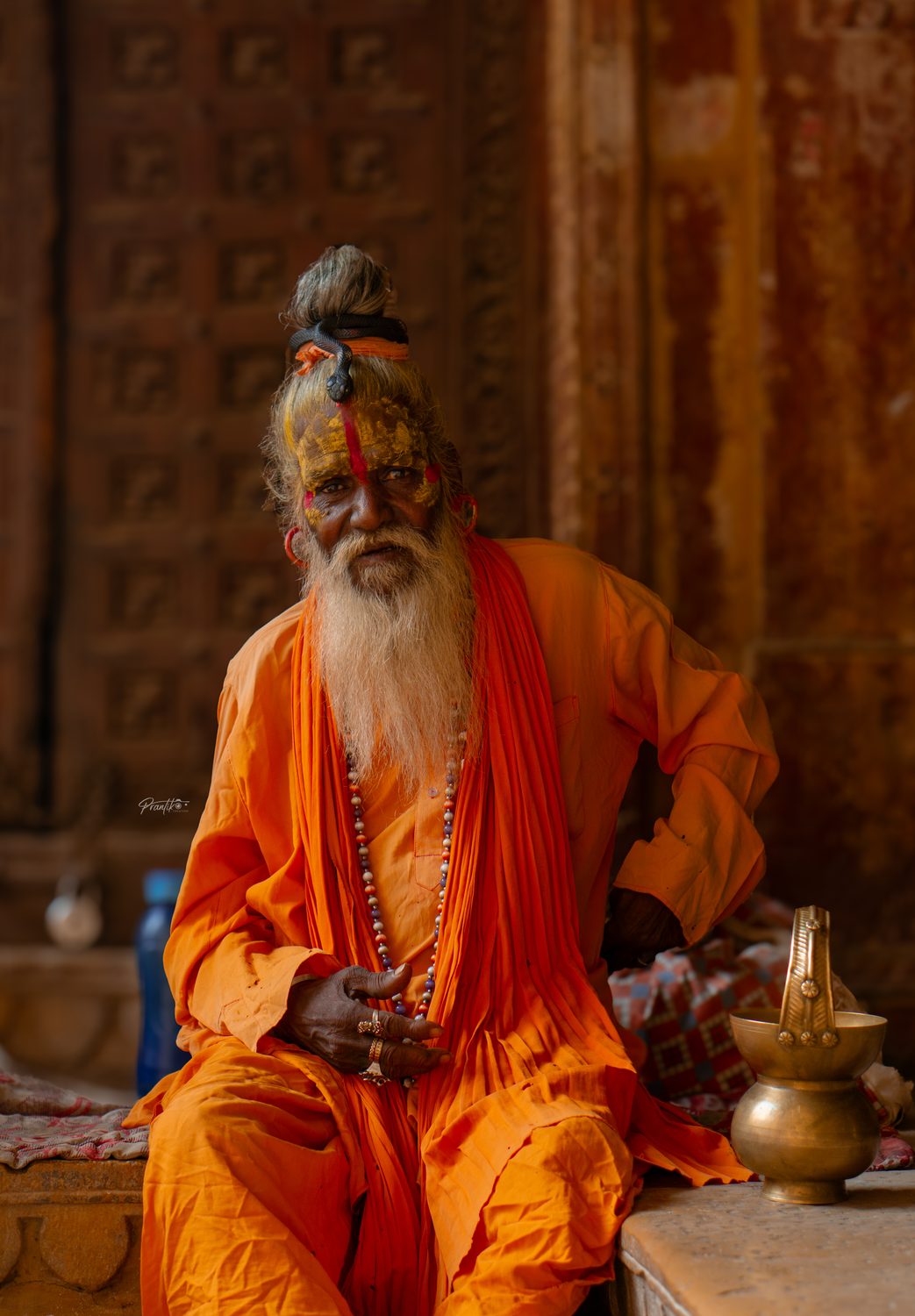 An elderly sadhu in saffron seated in a temple doorway